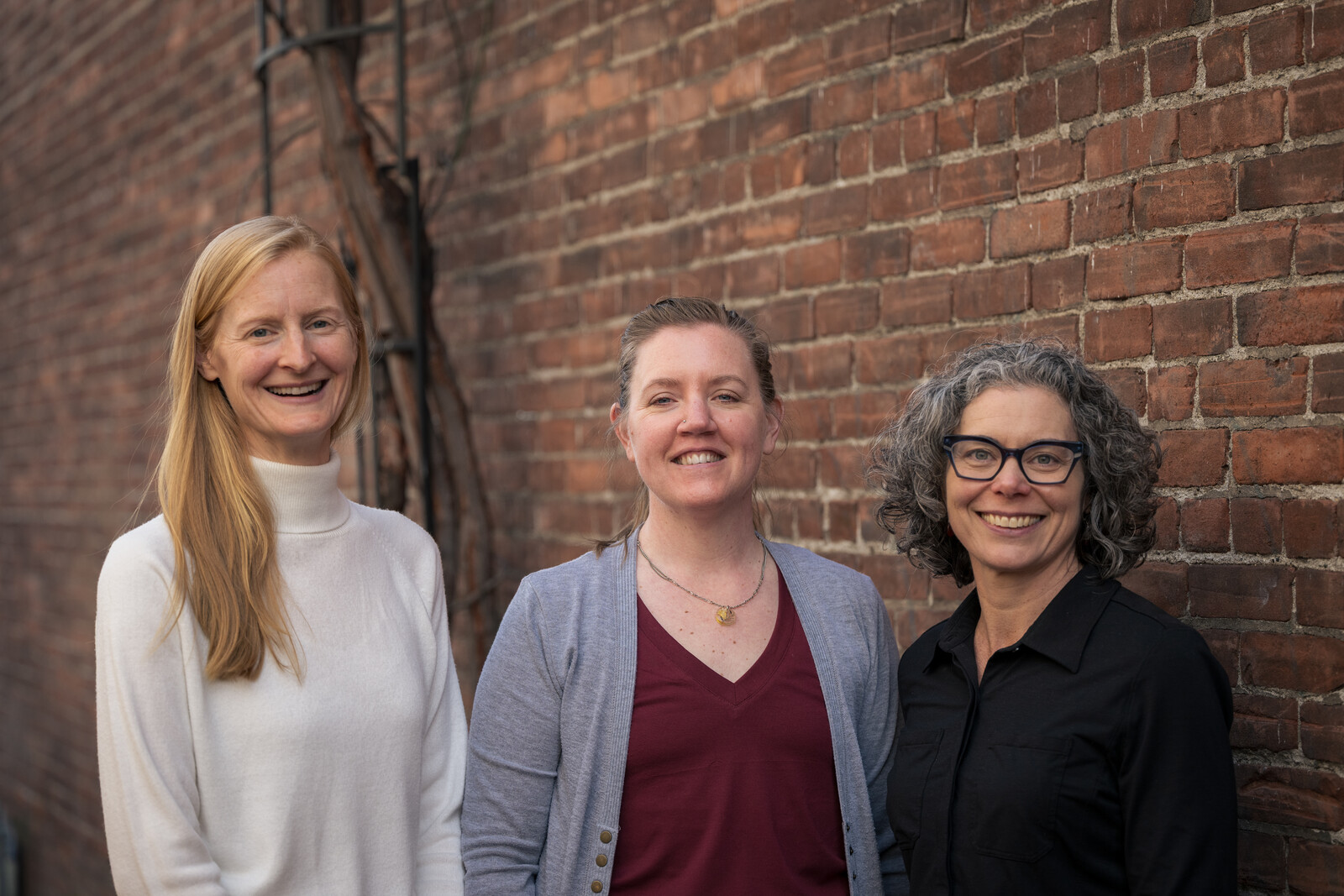 The three Excellence in Gyn founders smiling together in front of a brick wall