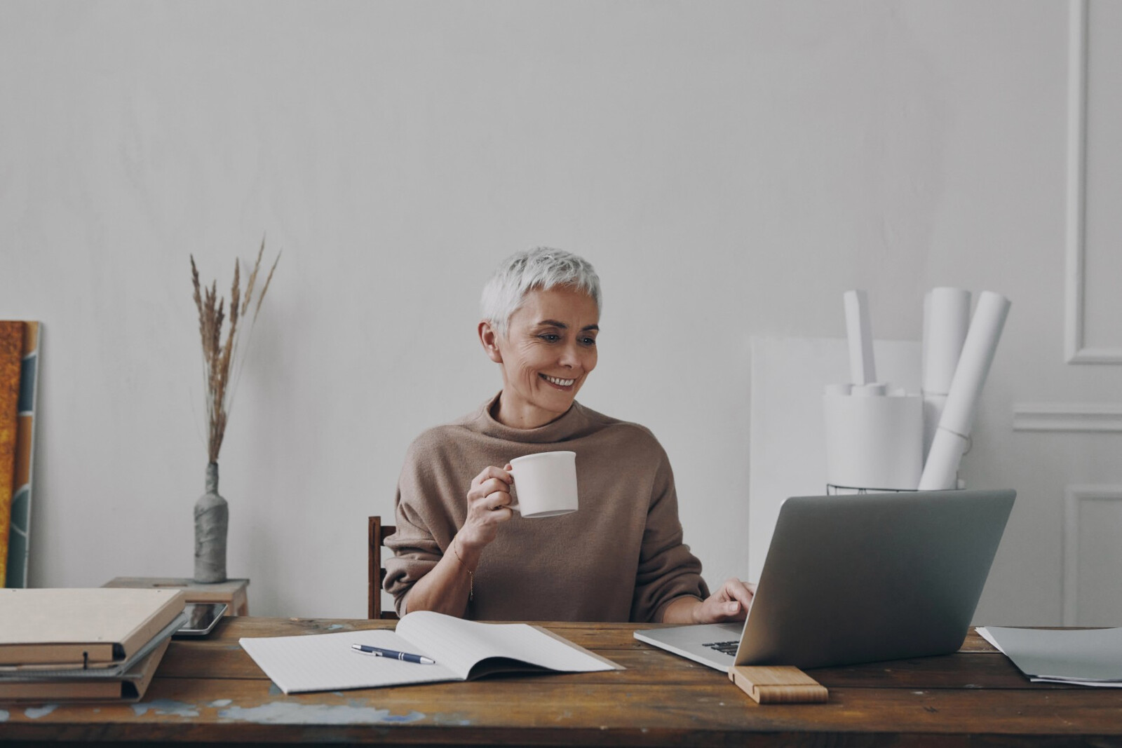Older person holding a mug with one hand and using a laptop with the other