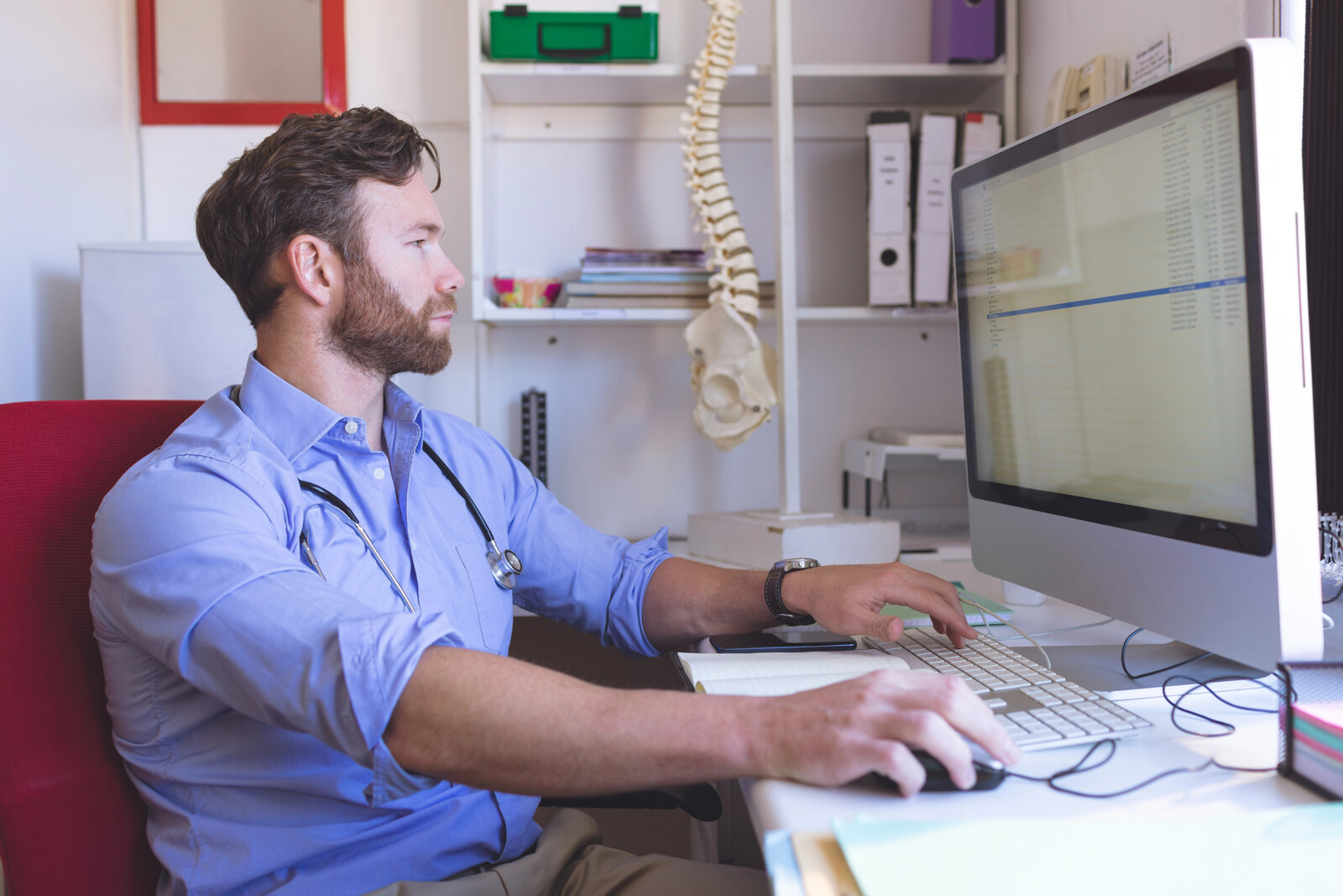 Clinician working at a desktop computer in an exam room with a spine model hanging nearby
