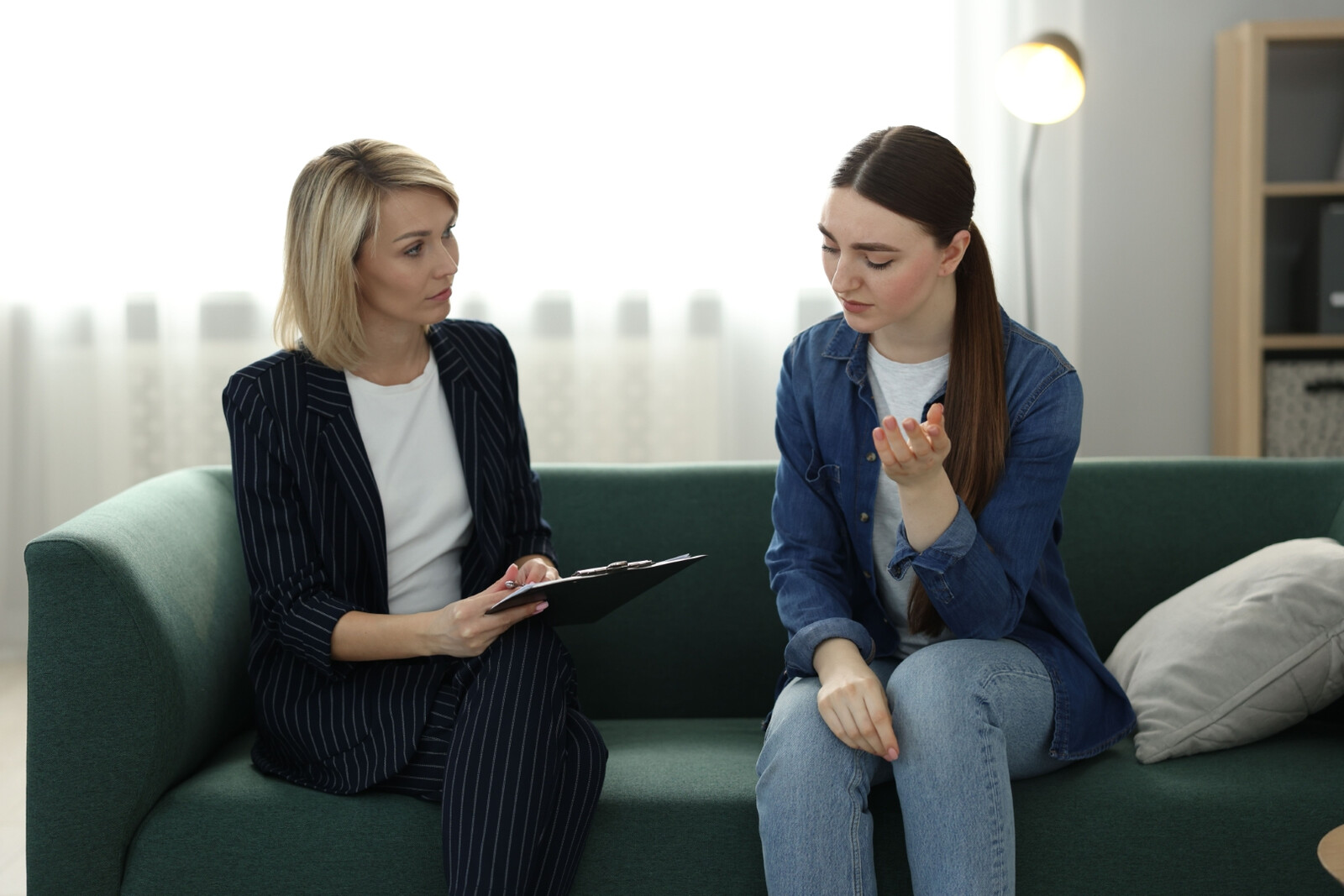 A clinician in a white coat sits across a desk from a patient, smiling and resting a reassuring hand on hers