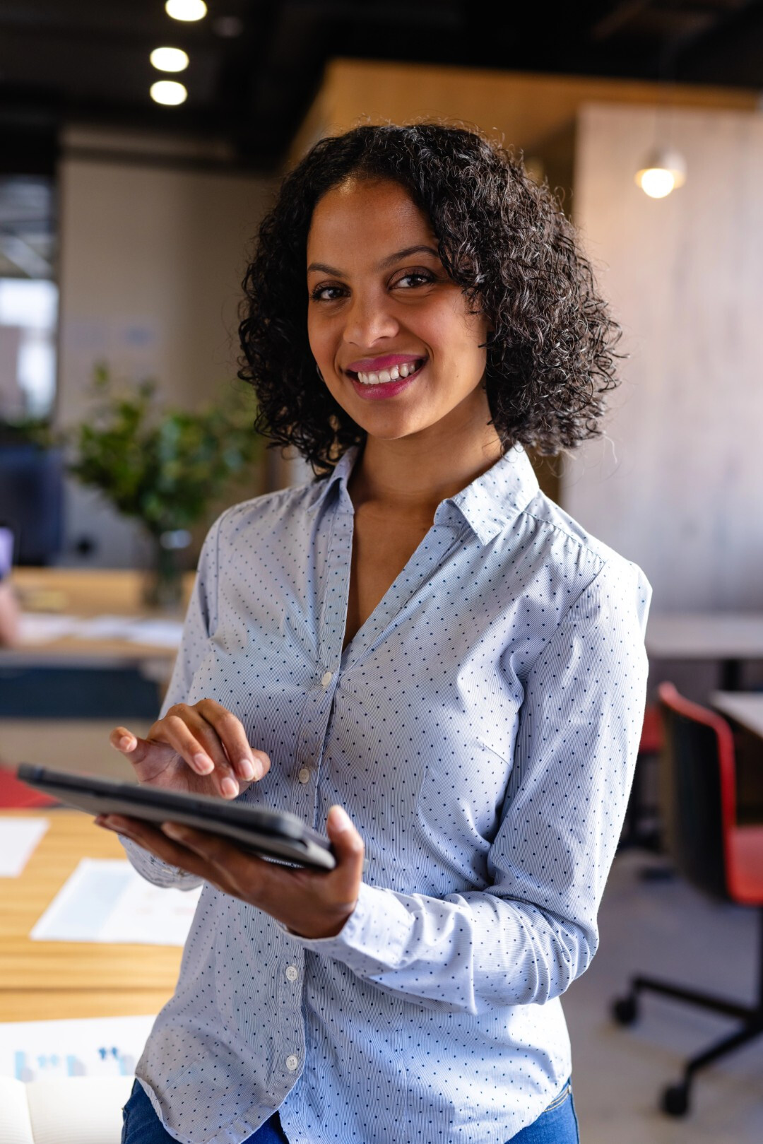 Smiling woman with curly hair using a tablet in a modern office